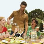 2 young smiling couples sitting at garden table, man pouring wine